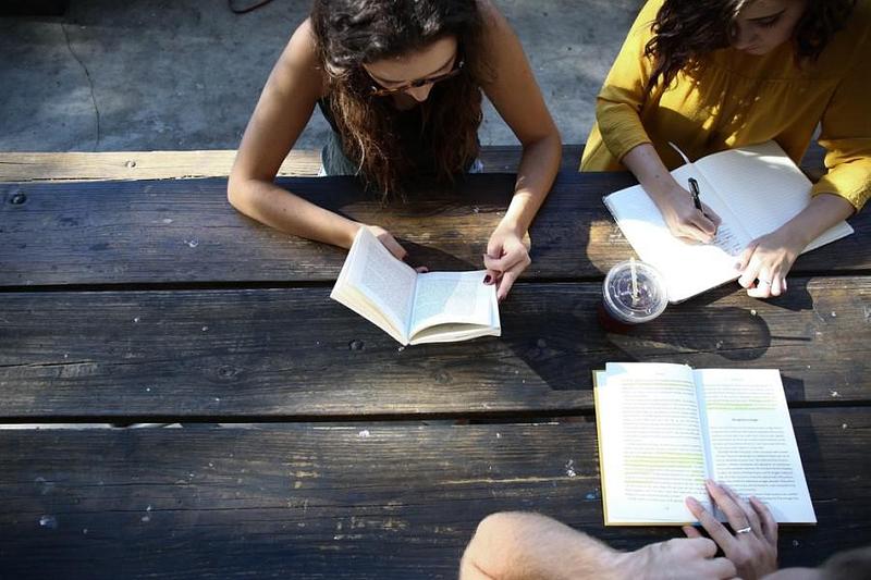 Three people sat at a picnic table reading and writing